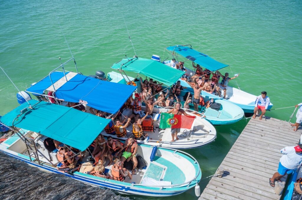 Bandeira de Portugal numa lancha com um grande grupo de pessoas em Holbox, sobre águas turquesa do Caribe.