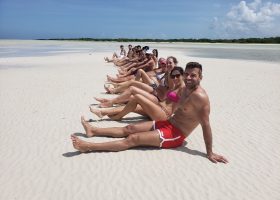 Pessoas a posar em Punta Mosquito, com águas rasas e paisagem paradisíaca ao fundo.