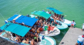 Bandeira de Portugal numa lancha com um grande grupo de pessoas em Holbox, sobre águas turquesa do Caribe.