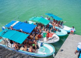 Bandeira de Portugal numa lancha com um grande grupo de pessoas em Holbox, sobre águas turquesa do Caribe.