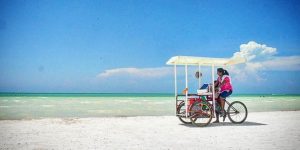 mulher em bicicleta na praia de holbox com areia branca e agua azul