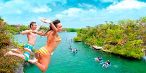 Pessoas a saltar para a água no Xel-Há, com lagoa cristalina e ambiente tropical ao redor.